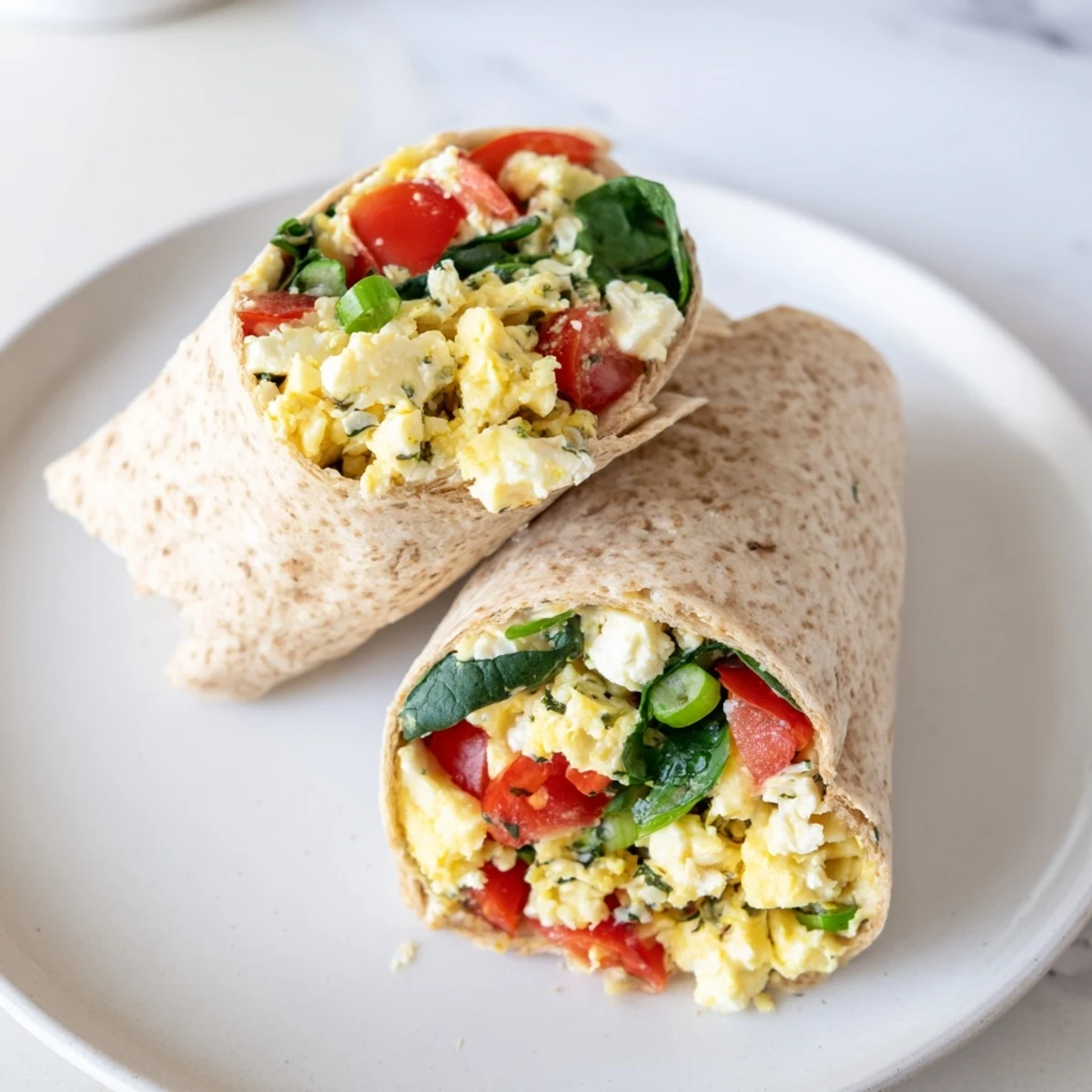 Golden feta egg wrap, fresh tomatoes and spinach visible inside a warm whole wheat tortilla.