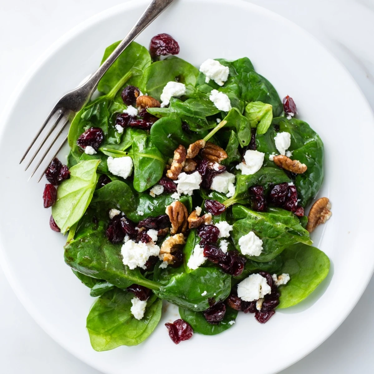 A vibrant Spinach Goat Cheese Salad with creamy crumbled cheese, sweet cranberries, and candied pecans on fresh spinach.