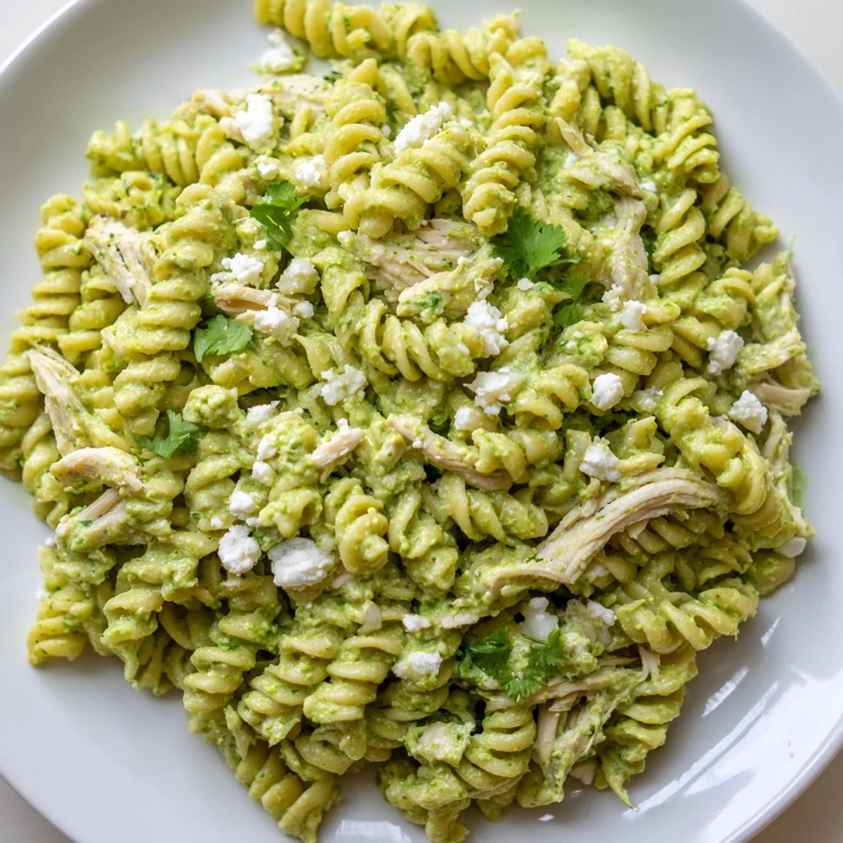 Fork-twirled rotini and shredded chicken swim in a tangy cilantro lime yogurt sauce, garnished with crumbled cotija.  