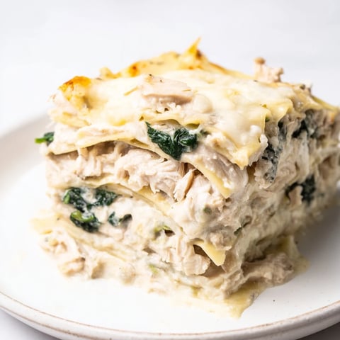A slice of creamy Chicken Alfredo Lasagna, layered with tender shredded chicken, ricotta, and melted mozzarella on a rustic plate.