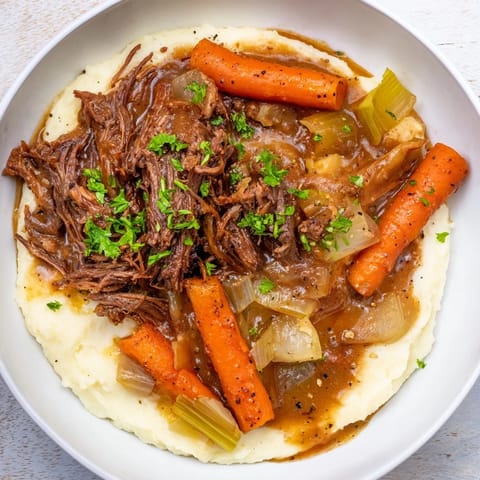 Juicy shredded Slow Cooker Pot Roast with vibrant carrots, onions, and creamy mashed potatoes.