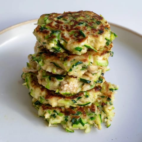Freshly made high-protein chicken zucchini fritters, ready to be served hot with a dollop of yogurt on top.
