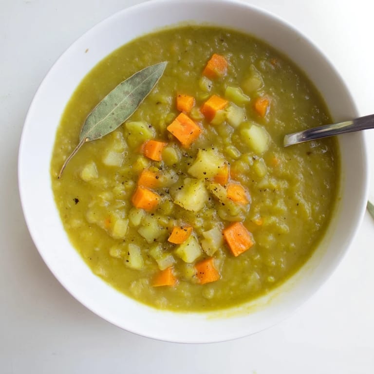 Steaming split pea soup with diced potatoes and celery in a rustic ceramic bowl for a cozy meal.