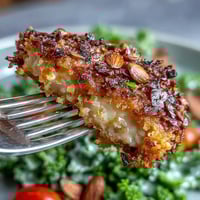 Golden-brown Almond-Crusted Chicken sizzling in a skillet, ready to serve alongside a vibrant kale and sumac salad.